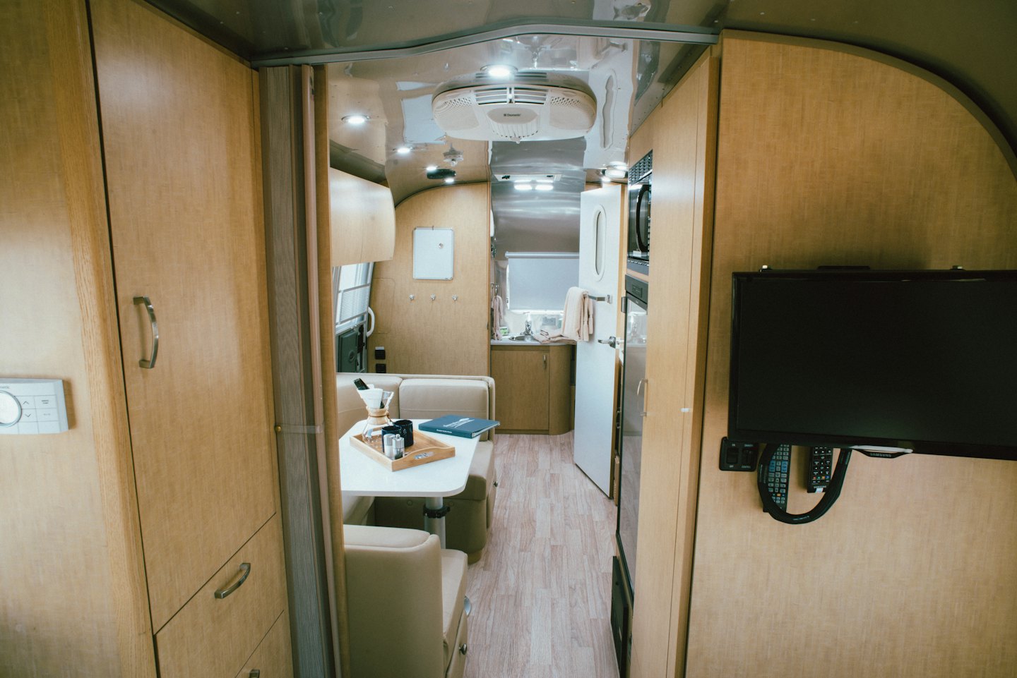Modern travel trailer interior with wooden cabinets and beige dinette seating.