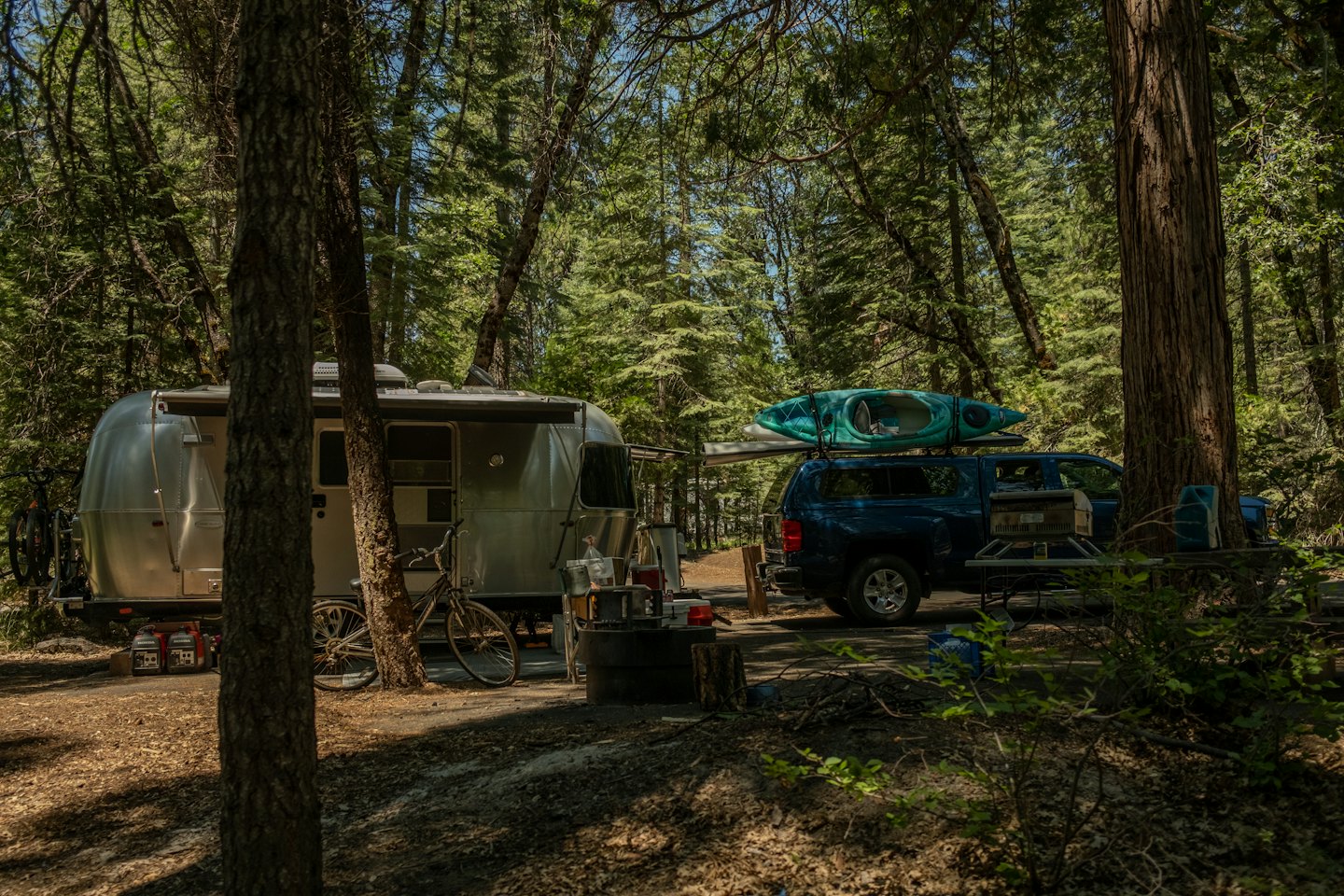 Silver Airstream trailer and pickup truck parked at a campsite.