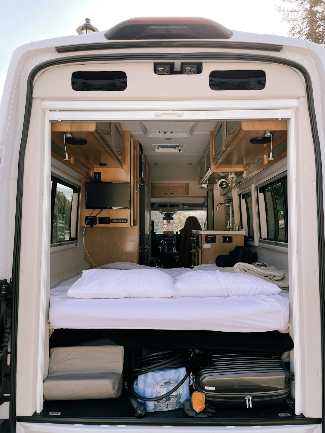 White camper van interior with a neatly made bed and cabinetry.